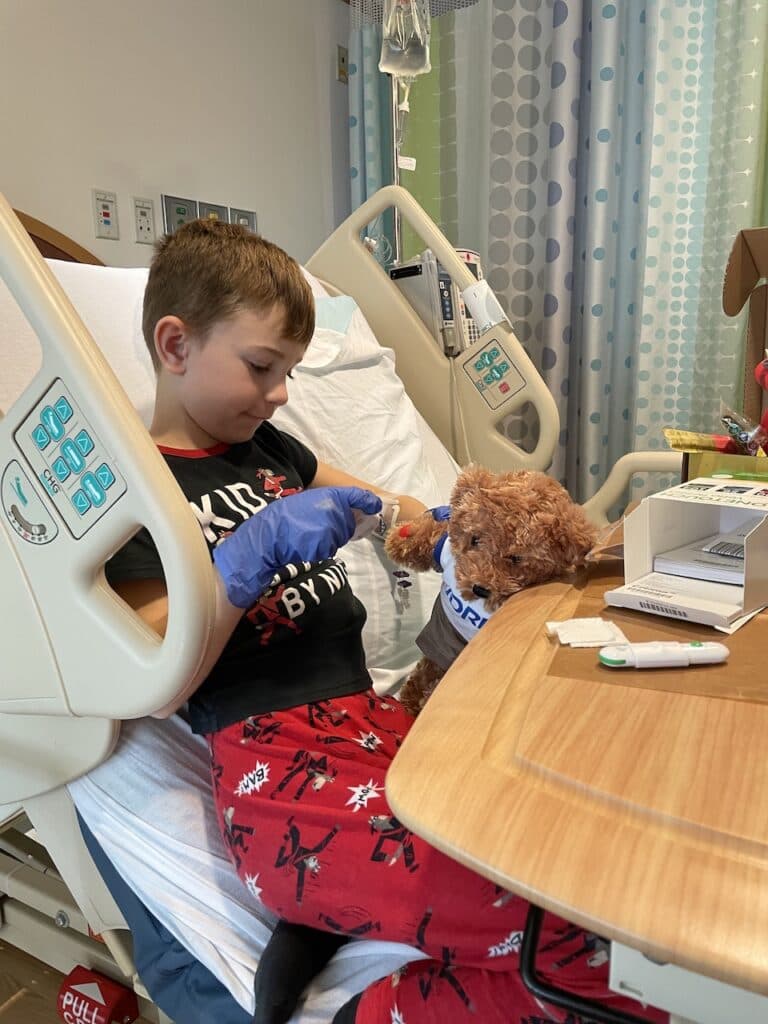 Bryson in a hospital bed practicing his daily diabetic care on his bear Rufus